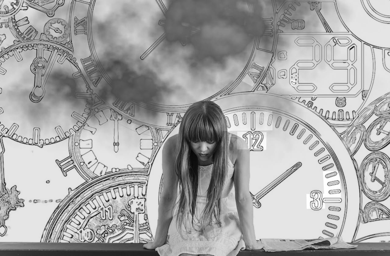Mujer cabizbaja sentada frente a un mural de relojes dibujados
