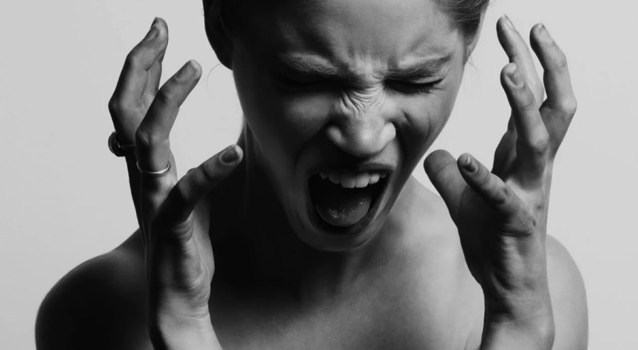 Mujer con los ojos cerrados y las manos tensas junto al rostro, en blanco y negro